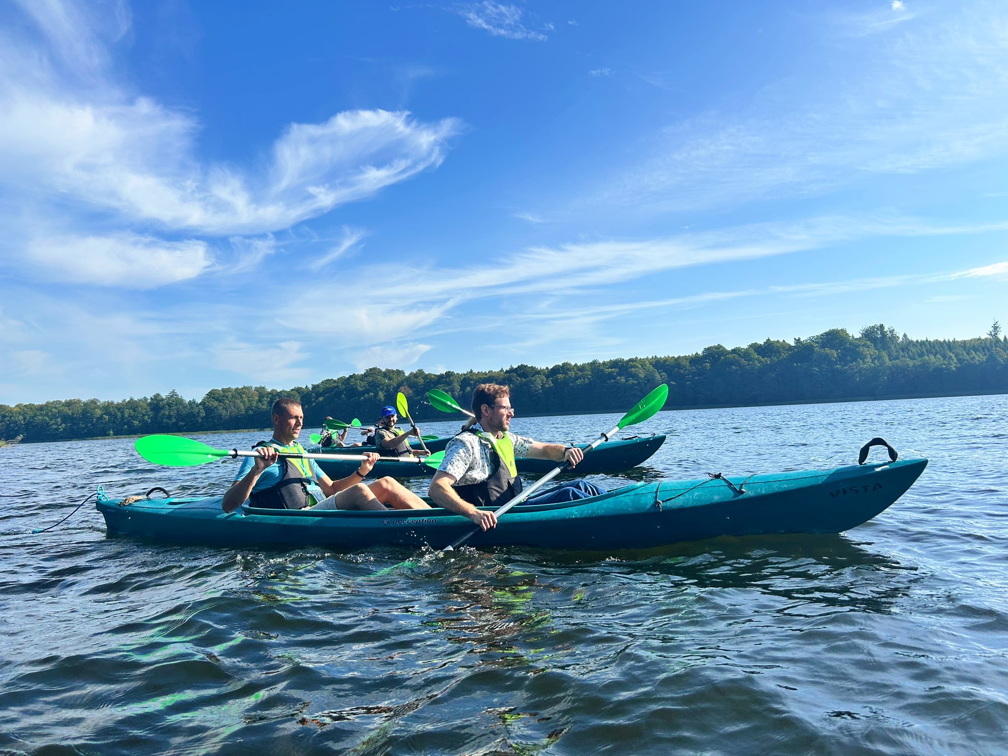 Two people kayaking on a lake under a clear blue sky.