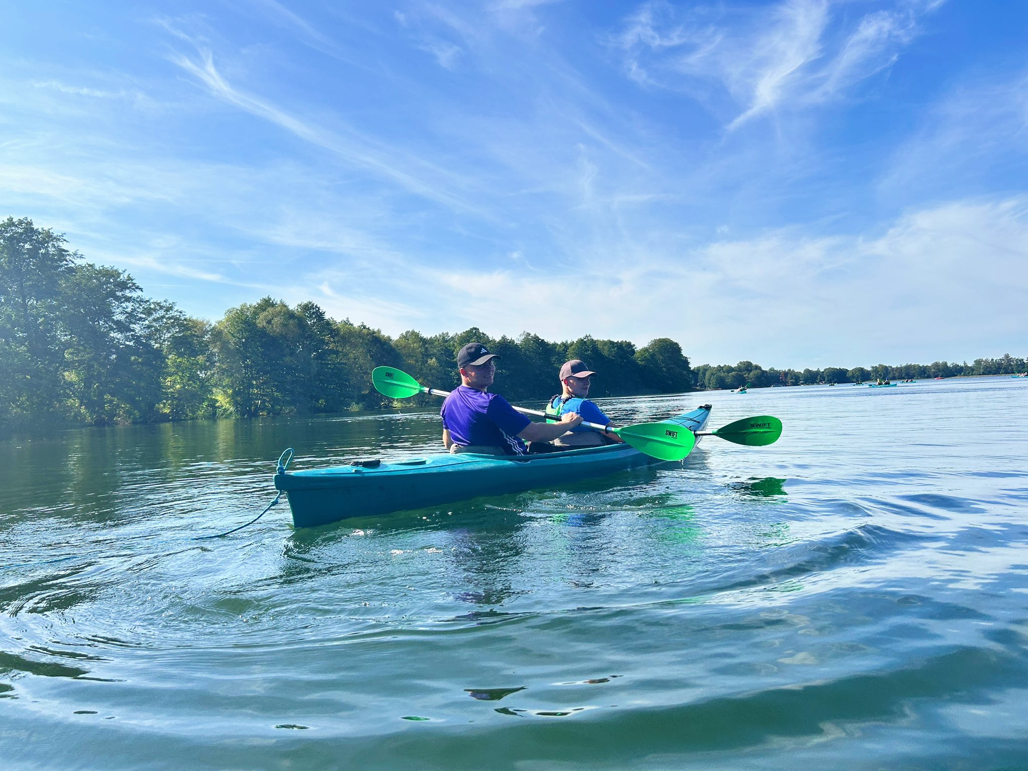 Two people kayaking on a calm lake under a clear blue sky.