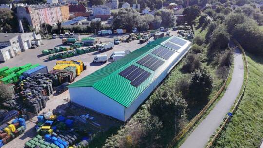 Aerial view of industrial facility with green roof and solar panels, surrounded by trees.
