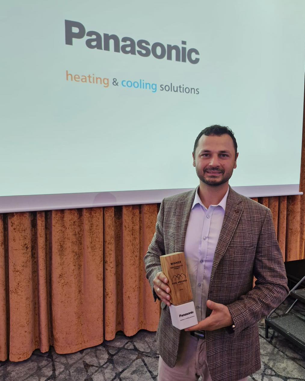 Man holding Panasonic PRO Awards trophy in front of branded presentation screen.