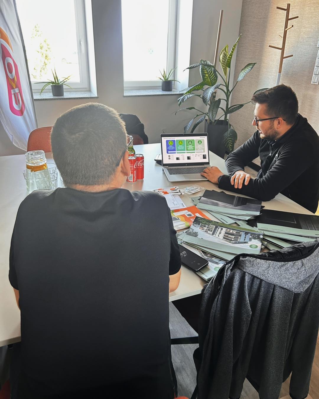 Two men at a table discussing a laptop presentation in a bright office.