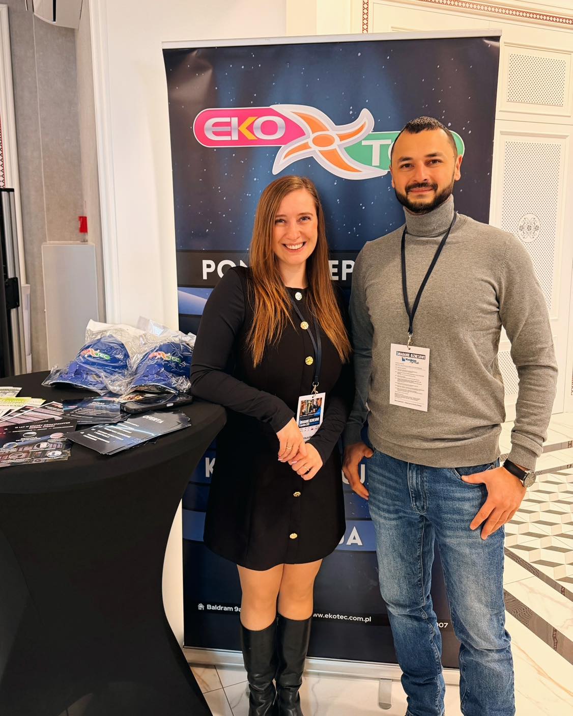 Two people smiling at a business event booth with promotional materials.