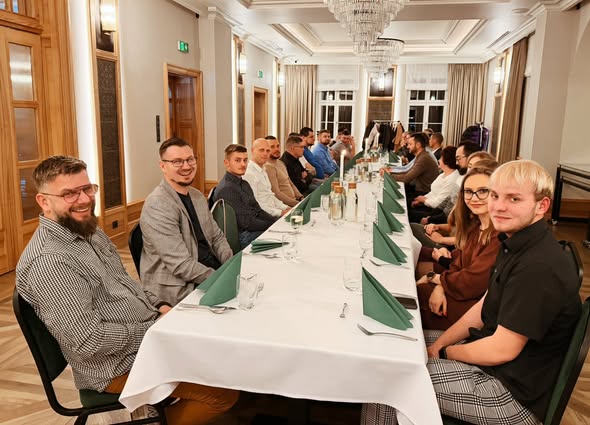 People seated at a long dining table with green napkins in an elegant room.