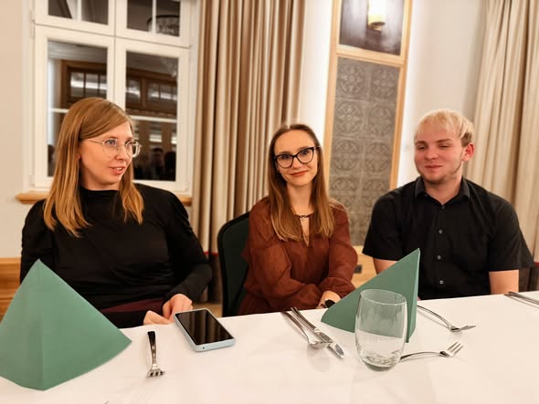 Three people sitting at a dining table with folded green napkins.