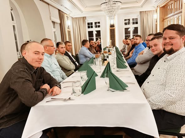 Group of people seated at a long dining table with green napkins.