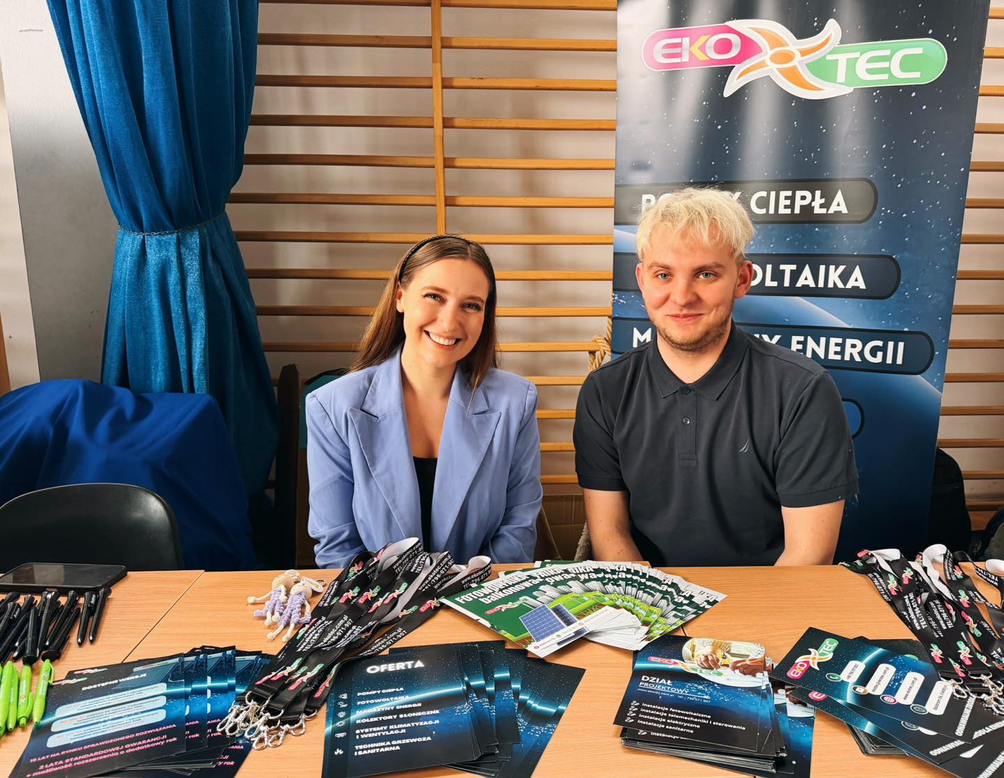 Two people smiling at a table with brochures and promotional items.