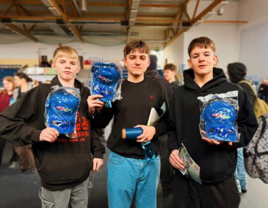 Three young people holding blue caps in a busy indoor setting.