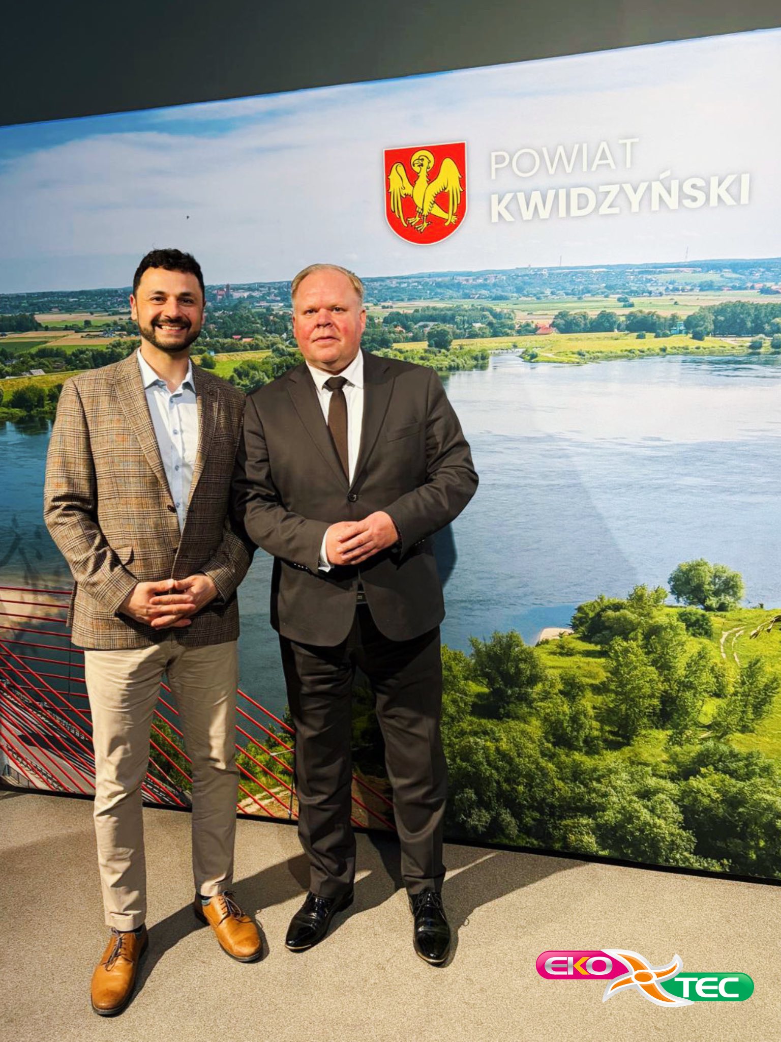 Two men in suits standing in front of Kwidzyński County backdrop.